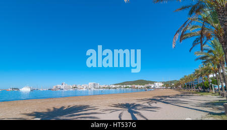 Sant Antoni de Portmany, Ibiza. La distanza in acqua e di un uomo le piastre una tavola a vela verso un veliero abbandonato, intrecciato sulla riva fino a venire. Foto Stock