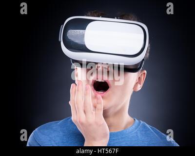 Stupiti teen boy urlando, indossando la realtà virtuale occhiali per guardare film o giocare con i videogiochi. Adolescente sorpreso cercando in VR bicchieri e shouti Foto Stock