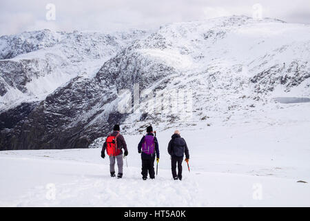 Tre escursionisti escursioni nella neve verso il basso Y Garn con vista Glyderau montagne del Parco Nazionale di Snowdonia. Ogwen, Gwynedd, il Galles del Nord, Regno Unito, Gran Bretagna Foto Stock