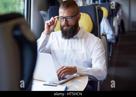 Uomo al lavoro su computer portatile presso il treno Foto Stock