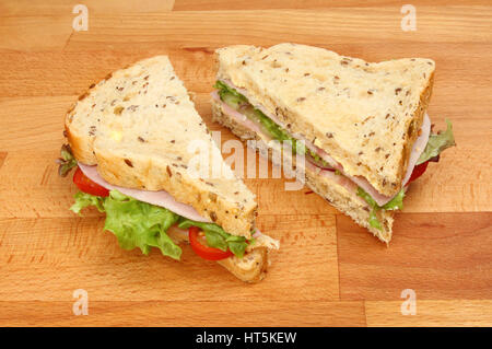 Due metà di un prosciutto sandwich insalata fatta con pane seminate su un tagliere di legno Foto Stock