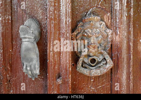 Vecchio doorknockers metallico in forma di lionhead e una mano umana collocata su un dipinto di marrone-vecchia mobilia di legno porta di una casa nella zona centrale di traino Foto Stock