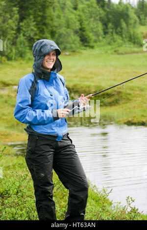 Donna con la canna da pesca in condizioni di tempo piovoso Foto Stock