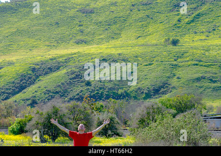 Uomo con le braccia spalancate in un campo aperto abbracciando la natura. Foto Stock
