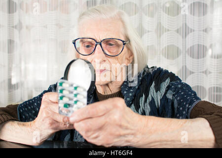 La nonna con lente di ingrandimento per determinare il nome del medicinale Foto Stock