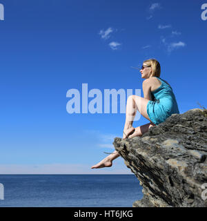 Donna seduta su roccia , guardando oceano, concetto di vacanza Foto Stock