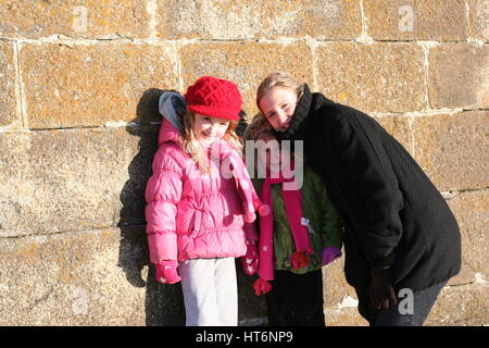 Bambine e la loro mamma in piedi da una parete in un freddo breezy day giornata con la famiglia, concetto, Irlanda, freddo, congelamento, Foto Stock