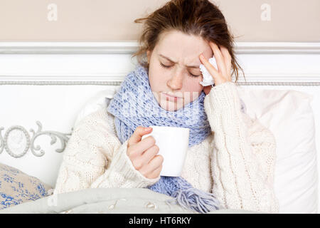 Malata con tazza di tè. Primo piano immagine di giovani frustrati donna in maglia Sciarpa blu tenendo una tazza di tè mentre è seduto nel letto della sua stanza. Foto Stock