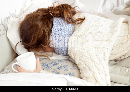 Malata con tazza di tè. Primo piano immagine di giovani frustrati malata in maglia Sciarpa blu tenendo una tazza di tè mentre giaceva a letto. Foto Stock