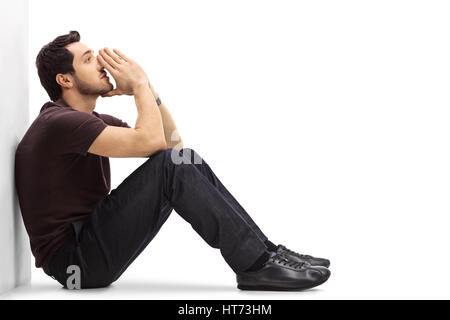 Malinconici uomo appoggiato contro una parete e il pensiero isolato su sfondo bianco Foto Stock