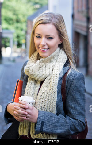 Un felice studentessa sorrisi a telecamera come essa si erge in una strada a ciottoli su una pausa dallo studio. Foto Stock