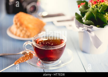 Un bicchiere di vetro di caldo fresco tè nero sul tavolo. Torta francese in background. Foto Stock