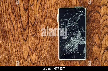 Vista dall'alto di Smartphone con schermo rotto su un tavolo di legno. Foto Stock