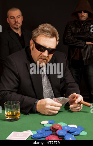 Foto di un uomo giocando a poker indossando occhiali da sole e fumare un sigaro. Foto Stock