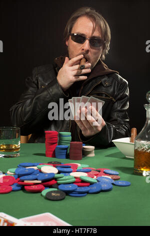 Foto di un uomo giocando a poker indossando occhiali da sole e fumare un sigaro. Foto Stock