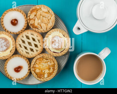 Piastra assortiti di singoli torte o crostate con una tazza di tè contro uno sfondo blu Foto Stock