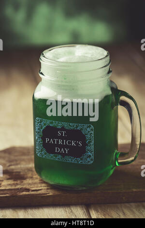 Primo piano di un muratore jar con tinta verde birra e il testo st. patricks giorno scritto in una etichetta attaccata ad essa, su una tavola di legno superficie rustico Foto Stock