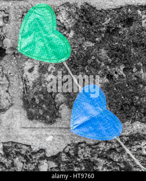 Due cuori uniti da una stringa uno verde e uno blu contro un muro grigio. Foto Stock