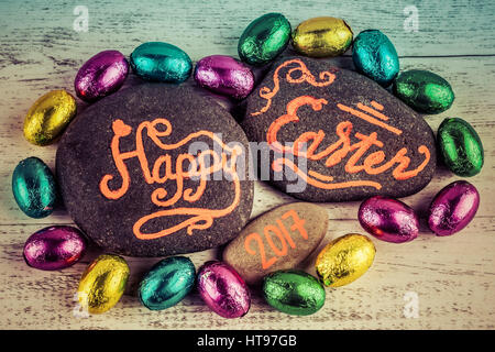 Felice Pasqua 2017 caratteri scritti su ciottoli con uova di cioccolato avvolto in foglio colorato. Immagine ha effetto vintage Foto Stock