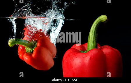 Splash acqua dall'acqua scende il peperone miscelata con attenzione un altro il peperone in sfondo nero con studio di illuminazione. in sfondo nero con s Foto Stock