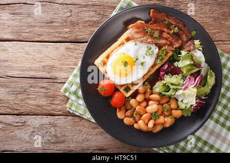 La deliziosa prima colazione: uovo fritto, cialde, pancetta, fagioli e insalata di close-up su una piastra orizzontale di vista da sopra Foto Stock