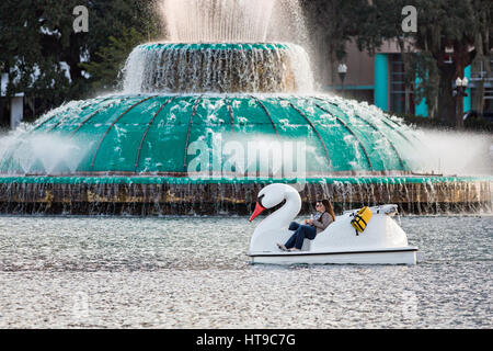 I turisti paddle Swan barche intorno Lake Eola Park passato il Linton E. Allen fontana commemorativa in Orlando, Florida. Lake Eola Park è situato nel cuore del centro cittadino di Orlando e casa di Walt Disney anfiteatro. Foto Stock