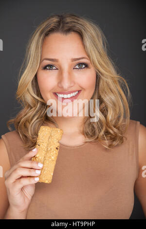 Bella bionda donna in piedi tenendo un cereali per la prima colazione bar. Foto Stock