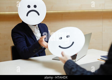 Vita-up verticale di imprenditore nasconde il suo volto sotto la maschera triste e raggiungendo la sua mano per prendere felice maschera dal suo collega, metafora concept Foto Stock