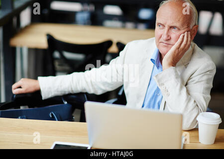 Ritratto di malinconico uomo maturo che poggia il capo sul lato cercando pensively lontano dalla telecamera mentre in seduta street cafe durante la pausa Foto Stock