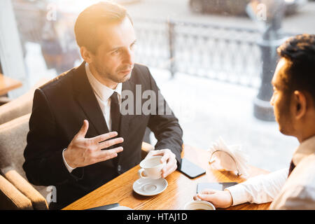 Angolo alto ritratto di successo di mezza età imprenditore che conduce i negoziati con il suo partner alla riunione in city cafe dalla calda luce del tramonto Foto Stock
