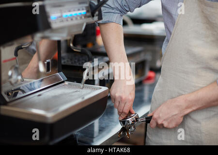 Giovane barista macinazione di chicchi di caffè in portafilter Foto Stock