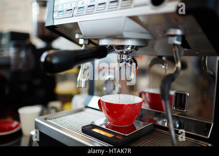 Espresso fresco versando in rosso caffè in tazza Foto Stock
