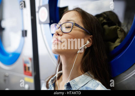 La ragazza di occhiali ascoltare musica durante l'attesa per i vestiti puliti Foto Stock
