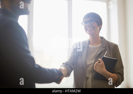 Fiducioso giovane imprenditrice indossando i capelli corti e occhiali stringono le mani con partner e sorridente dopo la firma di business di successo permanente della trattativa Foto Stock