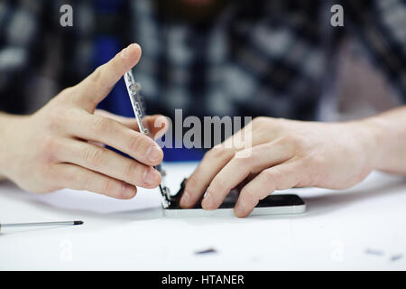 Closeup colpo di mani maschio coperchio di chiusura del telaio dello smartphone quando dopo il lavoro di riparazione sul tavolo bianco in officina Foto Stock