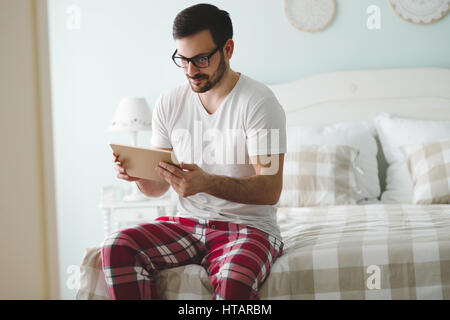 Uomo bello utilizzando compressa nella camera da letto indossando pigiami Foto Stock