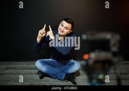 L uomo a concentrarsi sulla fotocamera digitale con schermo LCD agitando la mano mentre si è seduti a terra contro la parete per il concetto di blogging video Foto Stock