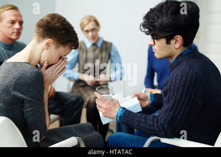 Giovane uomo di dare un bicchiere di acqua per groupmate durante la sessione di psicologico Foto Stock