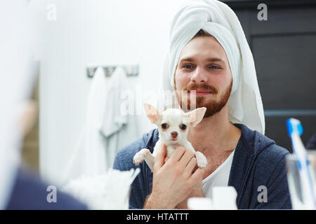 Uomo con asciugamano sul suo capo azienda chiwawa cucciolo nella parte anteriore dello specchio Foto Stock