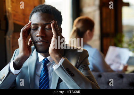 Ritratto di bello African American uomo che indossa business suit strofinando i suoi templi e chiudendo gli occhi affetti da mal di testa e affaticamento in tabella I Foto Stock