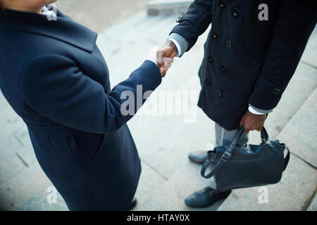 Sezione bassa ritratto di due irriconoscibile la gente di affari stringono le mani sulle fasi di costruzione di ufficio indossando cappotti Foto Stock