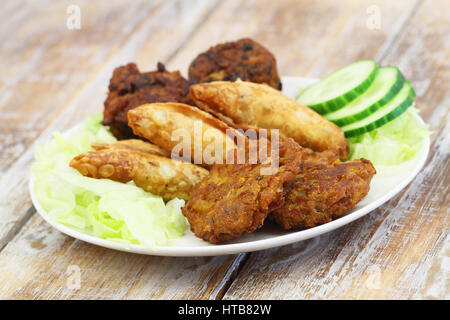 Spuntini Indiano comprese samosa, cipolla bhajis e pakoras sulla piastra bianca su una superficie di legno Foto Stock