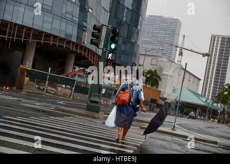 Honolulu, Hawaii, Stati Uniti d'America - 7 Agosto; 2016: una donna non identificato con ombrellone attraversando via sotto la pioggia sotto il cielo tempestoso di Honolulu e Oahu, Hawaii. Foto Stock