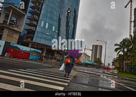 Honolulu, Hawaii, Stati Uniti d'America - 7 Agosto; 2016: una donna non identificato con ombrellone attraversando via sotto la pioggia sotto il cielo tempestoso di Honolulu e Oahu, Hawaii. Foto Stock