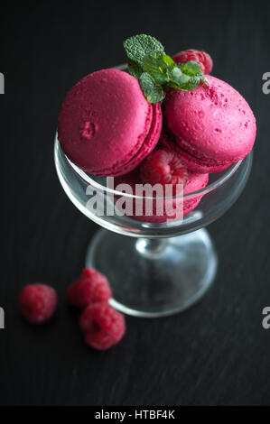 Amaretti rosa con lamponi in coppa su sfondo nero Foto Stock