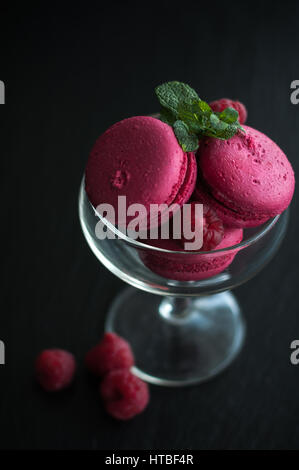 Amaretti rosa con lamponi in coppa su sfondo nero Foto Stock