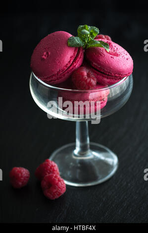 Amaretti rosa con lamponi in coppa su sfondo nero Foto Stock