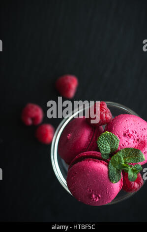 Amaretti rosa con lamponi in coppa su sfondo nero Foto Stock