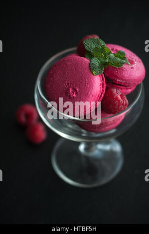 Amaretti rosa con lamponi in coppa su sfondo nero Foto Stock