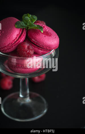 Amaretti rosa con lamponi in coppa su sfondo nero Foto Stock